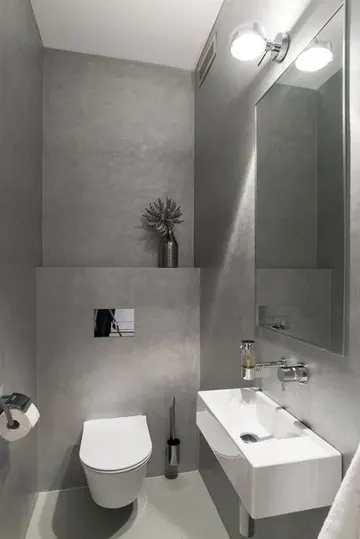 Betonla yapılmış minimalizm örneği bir misafir tuvaleti, duvara monte lavabo, lamba ve büyük ayna ile.