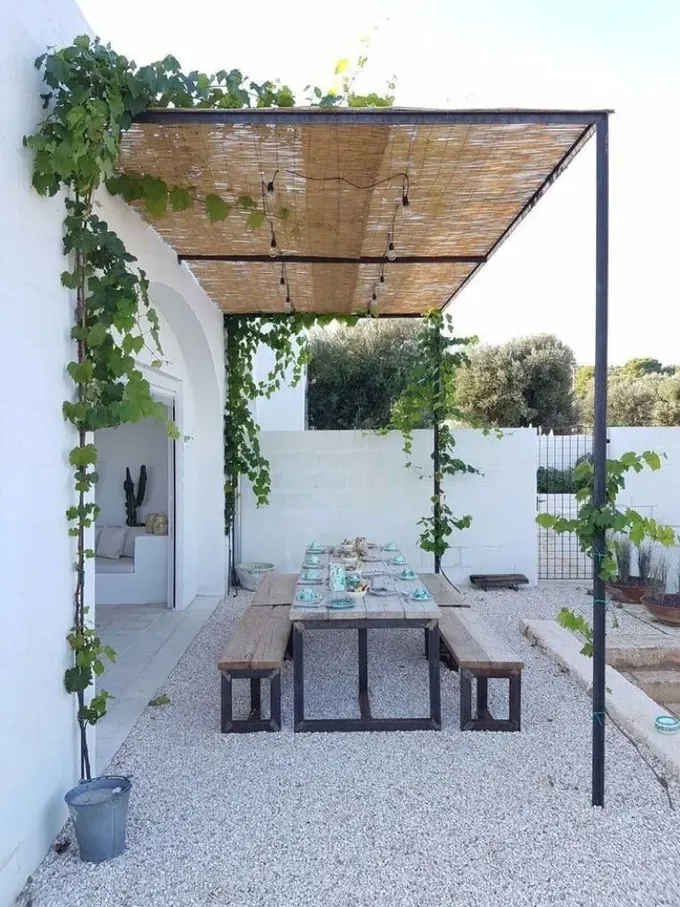 Işıklar ve sarmaşıklarla kaplı hasır pergola, açık hava yemek alanı için şık bir çözüm.