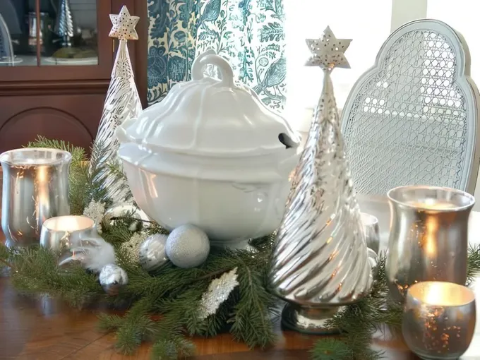 Cıva camdan ağaçlar, mumluklar, gümüş süslerle tamamlanmış yeşilliklerden oluşan şık ve parlak gümüş bir Noel masa ortası.