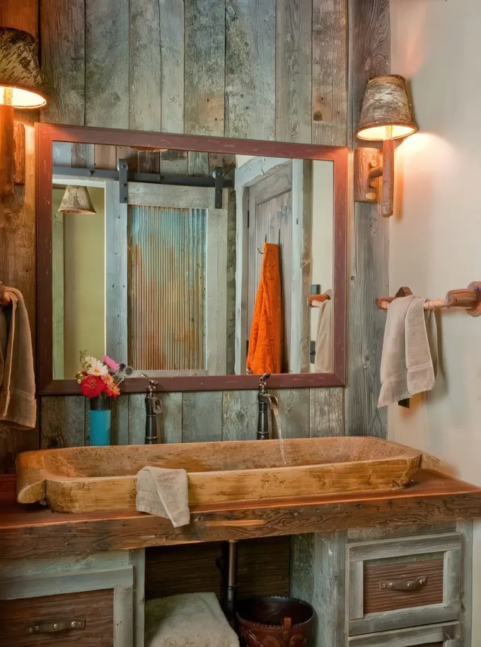 Geri dönüştürülmüş ahşap kaplama, çerçeveli büyük ayna ve taş lavabolu geniş bir banyo dolabı olan ahır banyosu.