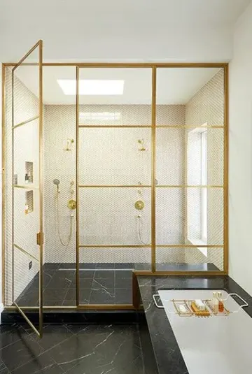 Siyah mermer ve küçük yuvarlak karolarla yapılmış gösterişli ve sofistike banyo, altın çerçeveli cam kapılı duş alanı.