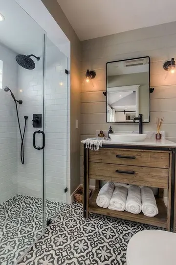 Nötr ve desenli zemin karoları, ahşap lavabo ve siyah armatürlerin bulunduğu küçük çiftlik evi tarzı banyo.