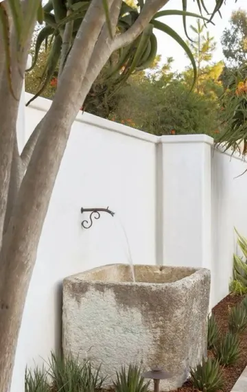 Sazlık ve ışıklar, çeşmenin gizlendiği çit kenarındaki oluğa hoş bir dokunuş katar.