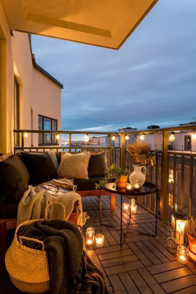 Balkon modern dış mekan mobilyaları, çok sayıda mum ve korkulukta birkaç ampulle düzenlenmiş.