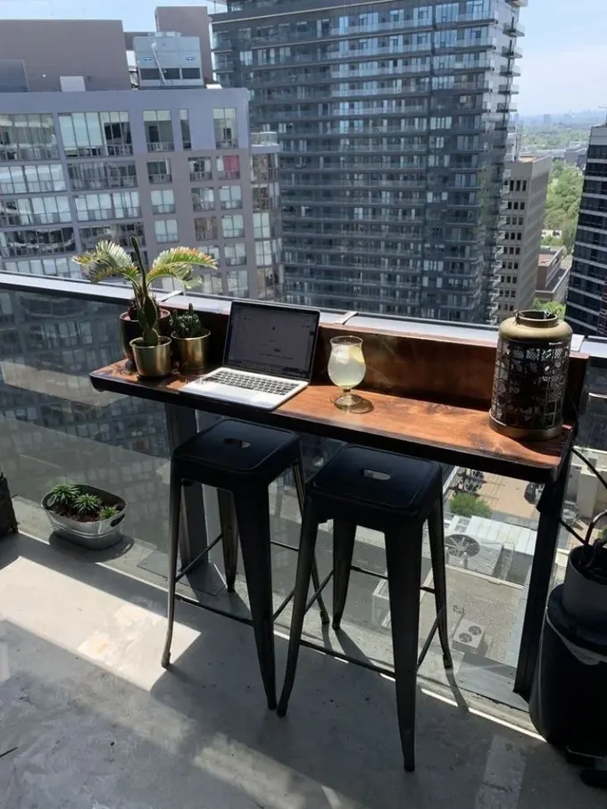 Küçük balkon, korkuluk mini masası, iki siyah tabure, dizüstü bilgisayar ve bazı dekorlarla göz dolduruyor.