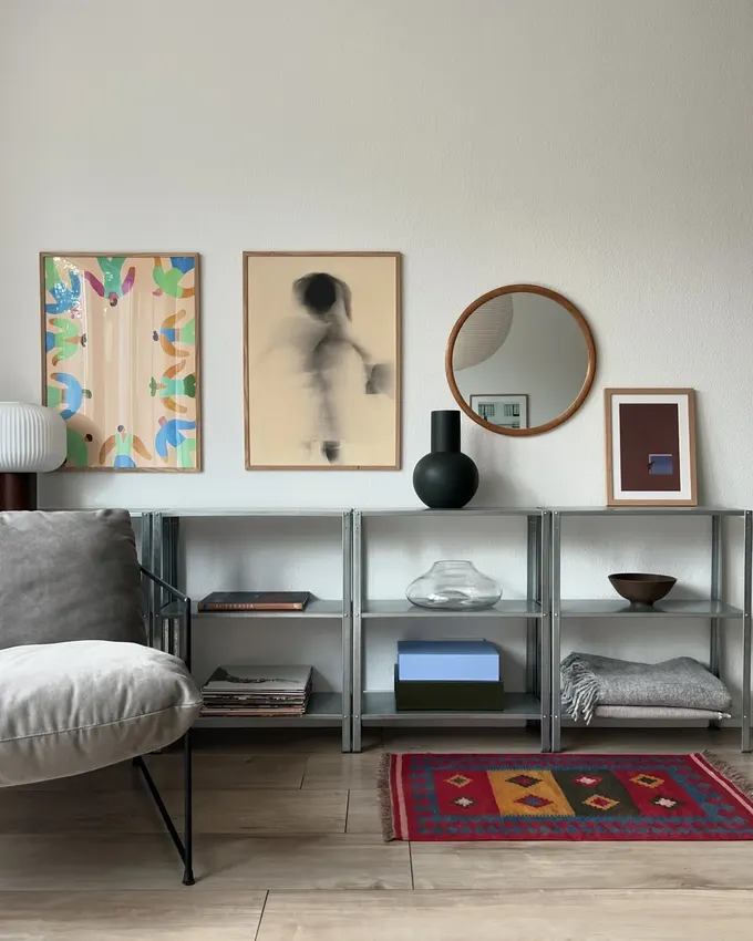 Modern bir oturma odasında alçak IKEA Hyllis rafları, kitap, vazo ve duvar sanatı ile minimalist bir görünüm sunuyor.