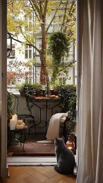 Küçük balkon, zarif antika dövme mobilyalar, bolca yeşillik, yapraklar ve balkabağıyla dekore edilmiş.