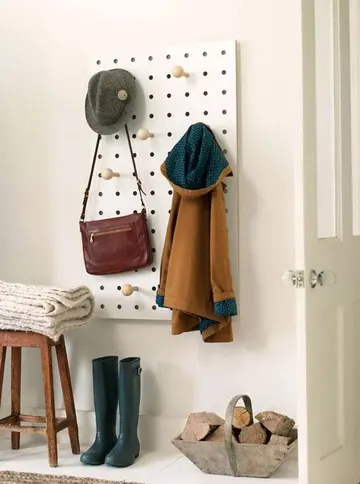 Küçük beyaz pegboard ve tabure girişte depolama için kullanılmış, odun ve lastik botlar dekor olarak eklenmiş.