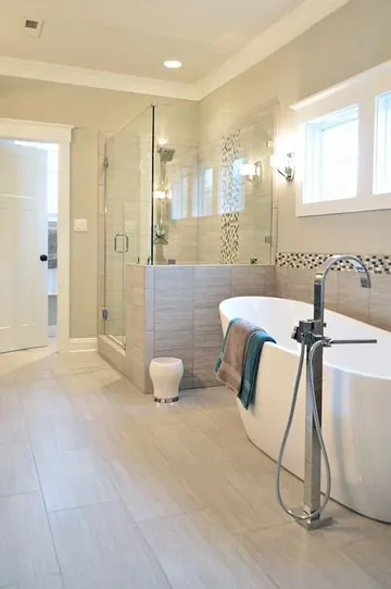Sandy karolarla kaplı şık, modern banyo; ışık alan yarım duvarlı duş ve güzel bir küvet.