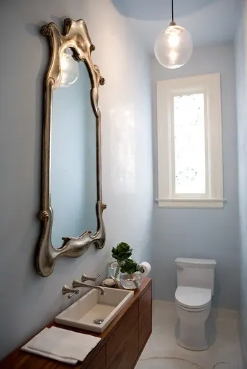 Pastel mavi misafir tuvaleti, büyük ahşap lavabo, vintage çerçeveli ayna ve sarkıt lamba ile.