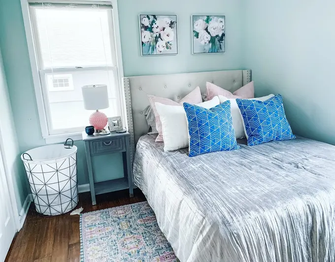 Bu huzurlu yatak odası, pastel mavi duvarlar, parlak beyaz nevresimler ve narin çiçek detaylarıyla küçük bir odayı daha geniş hissettiriyor. Minimalist ve ferah tasarımlar için ideal.