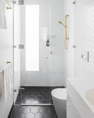 Beyaz kılçık ve siyah altıgen fayanslı küçük banyo. Sırttan buzlu pencere ve altın armatürler mevcut.