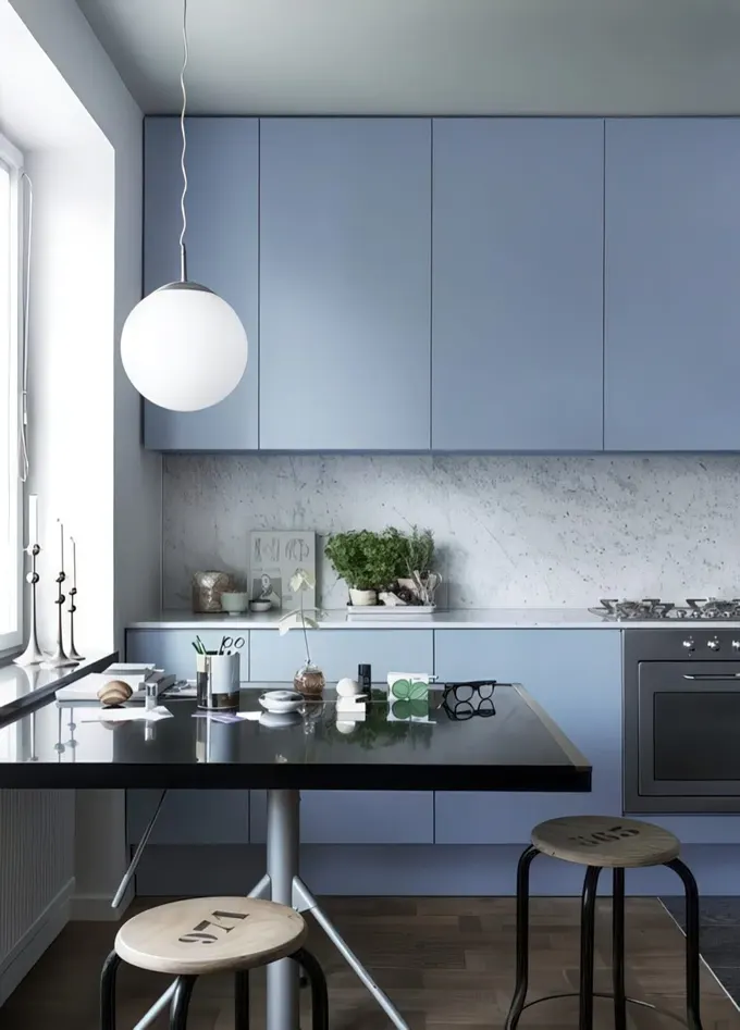 Endüstriyel tabureler ve siyah masa ile tamamlanmış gri taş sırtlık ve tezgahlı minimalist açık mavi mutfak.