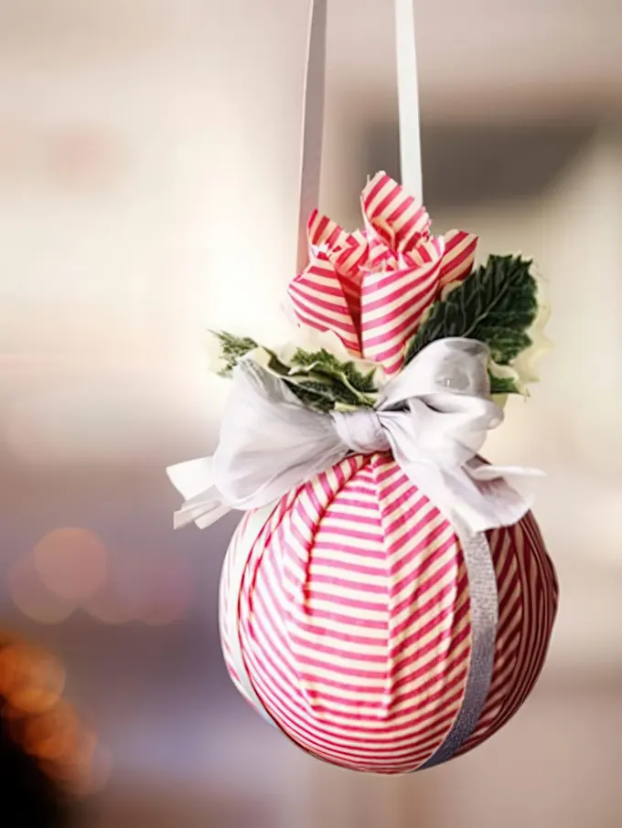 Kırmızı beyaz çizgili Noel süsü, yeşillik ve beyaz kurdele fiyonkuyla gerçekleştirilebilecek geleneksel bir fikir.