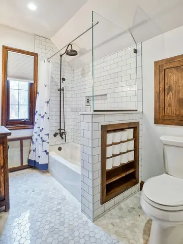 Beyaz ve mermer karolarla vintage ilhamlı banyo, entegre depolama alanlı yarım duvar ve sıcaklık katan eskitilmiş ahşap dokunuşlar.