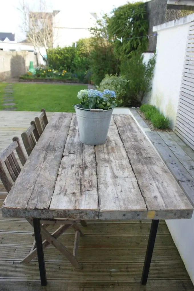 Bu geri kazanılmış ahşap masa, shabby chic sandalyelerle uyumlu, yemekhane alanı ise yeşilliklerle çevrili.