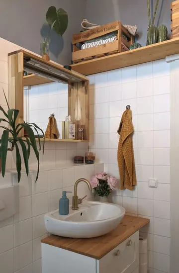 Banyo, boyalı ahşap kullanılarak yapılmış ve üzerindeki açık raf hem saklama hem dekor için değerlendirilmiş.