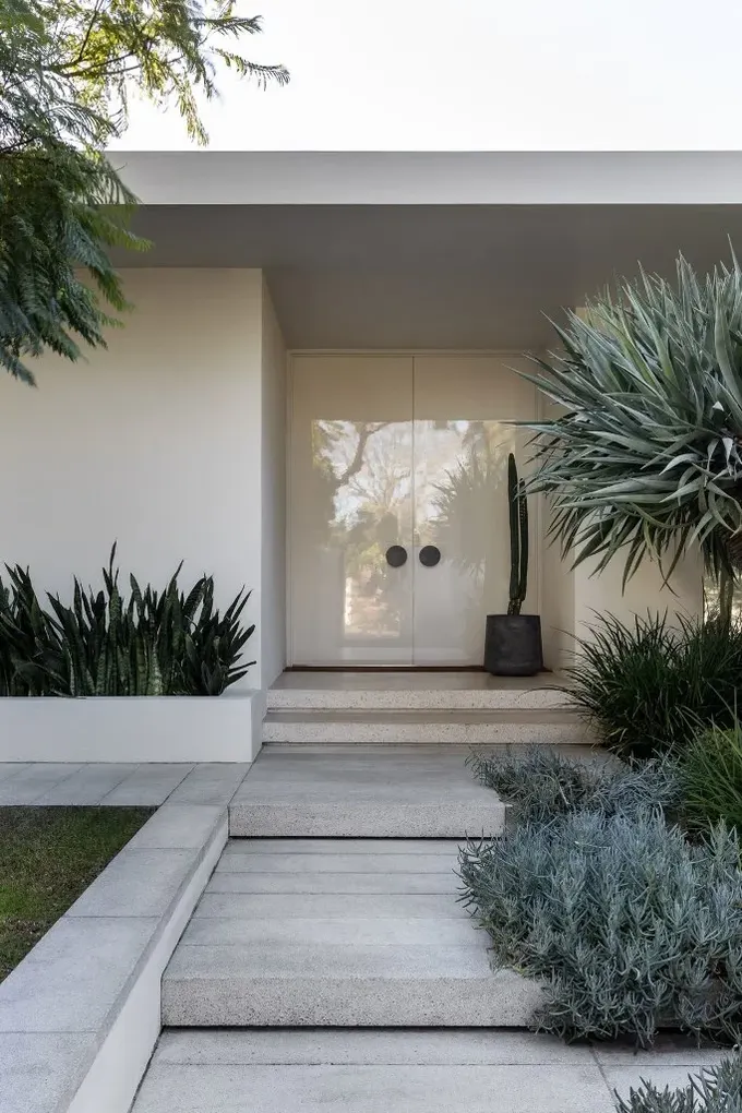 Minimalist ön bahçede, ağaç, otlar ve sukulentlerle birlikte gömme bahçe yatakları ve çim alan var.