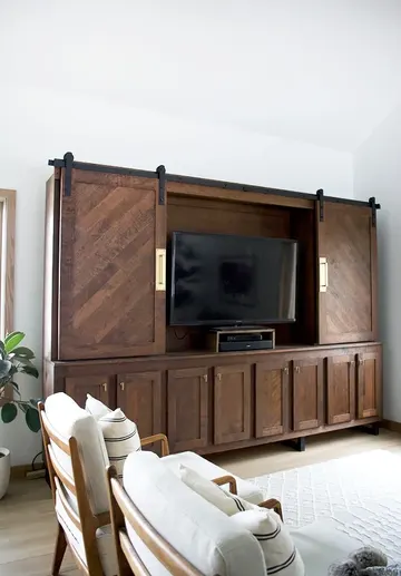 Koyu renkli, vintage tarzda ve sürgülü kapaklı şık bir dolap; TV'yi gizlerken şıklığını ortaya koyuyor.