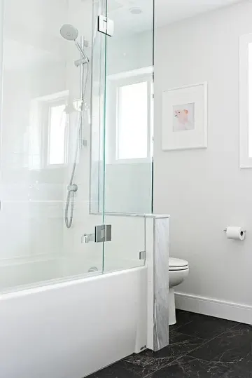 Siyah zeminli minimalist banyo, yarım duvar tuvaleti ayırıyor, duş ve küvet alanı bir arada.