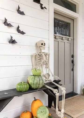 Eskitilmiş balkabakları, iskelet ve duvardaki yarasalarla rustik tarzda bir Halloween verandası.