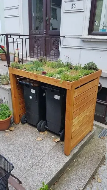Kapak, boyalı ahşaptan yapılmış ve üstünde yeşillik ve sukulentlerle dolu bir tepsi var.