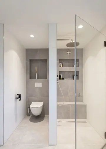 Minimalist gri ve nötr fayanslı banyo, nişli duş alanı, kesintisiz cam kapı ve nötr cihazlar.