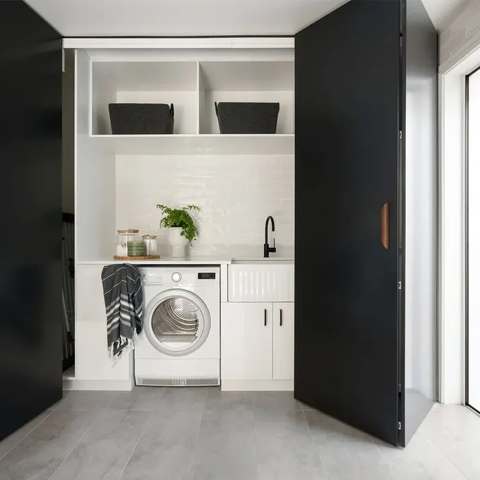Koyu renk, minimalist çift katlı kapakların arkasında akıllıca gizlenmiş çamaşır alanı. Kapalıyken modern ve düzenli görünür.
