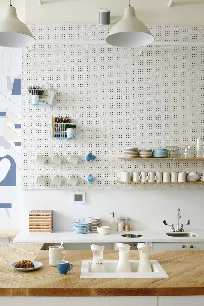 Beyaz büyük pegboard duvar, üst dolaplardan daha hafif görünür ve tavan hizasına kadar kullanılabilir.