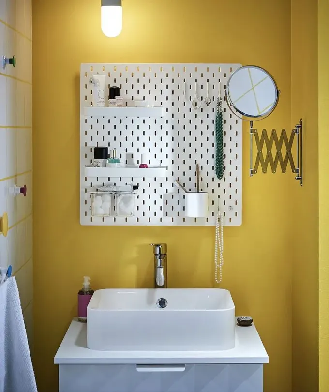 Beyaz pegboard, sarı duvarda öne çıkar ve kullanışlı depolama alanı sağlar.
