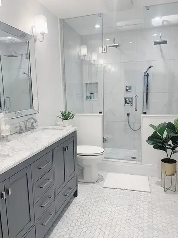 Mermer altıgen fayanslarla kaplı modern nötr banyo, yarım duvarlı duş, gri lavabo ve büyük ayna içeriyor.