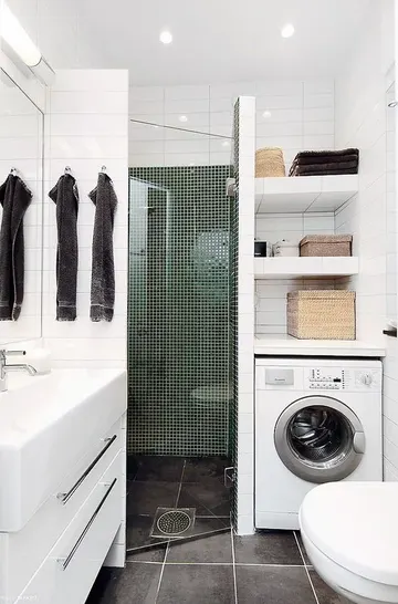 Seramik döşeli duş alanı, çamaşır makinesi, beyaz lavabo ve tezgâh olan çağdaş küçük banyo.