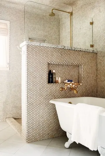 Duvarlarda gri ve küçük yuvarlak seramikler, pony duvar, pirinç detaylar ve vintage bir küvetin bulunduğu şık banyo.