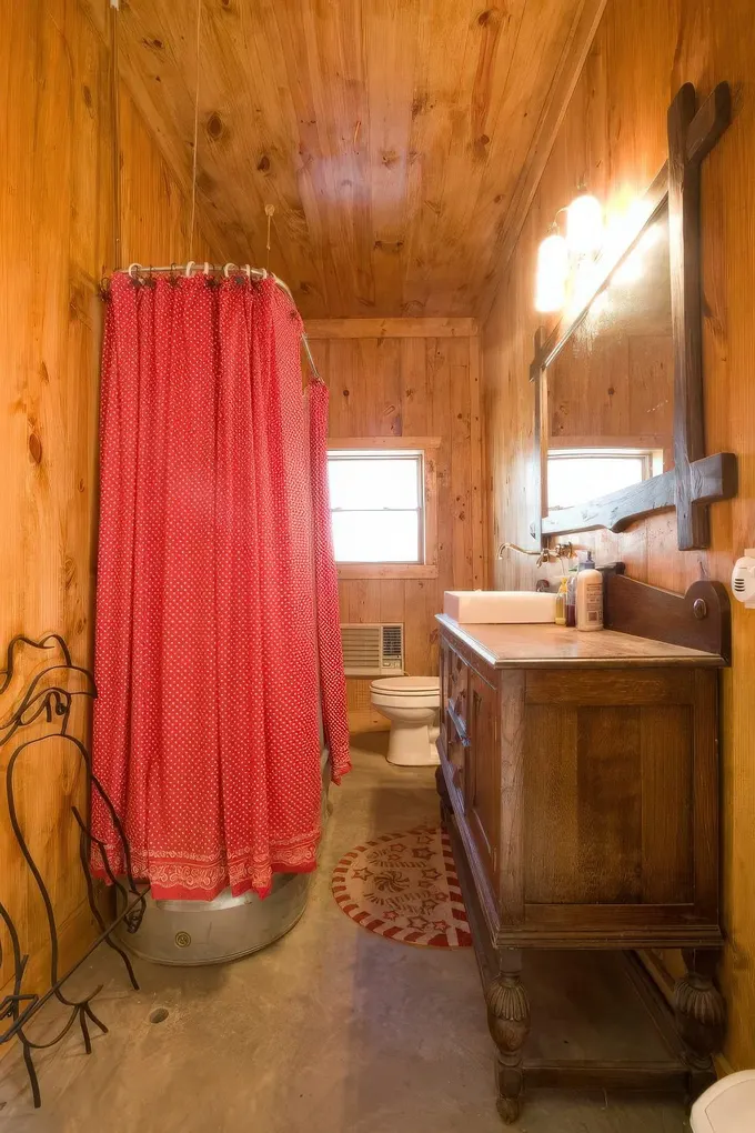 Ahşap kaplamalı sıcak bir ahır banyosu, ahşap lavabo dolabı, büyük ayna, metal küvet ve parlak kırmızı perde.