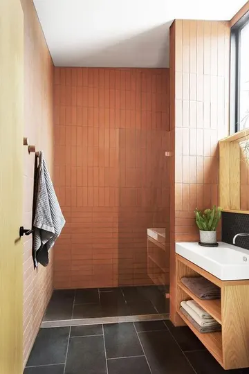 Turuncu ve sarı duvarlar, siyah zemin karoları, lekeli lavabo ve beyaz cihazlar ile aydınlık banyo.