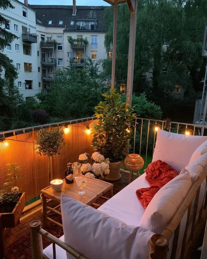 Balkon, rattan mobilyalar, saksı bitkileri ve dekoratif süs dizileriyle düzenlenmiş.