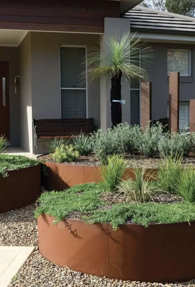 Modern ön bahçe, corten çelik kenarlıklı üç yuvarlak bahçe yatağı ve yeşilliklerle düzenlenmiş.