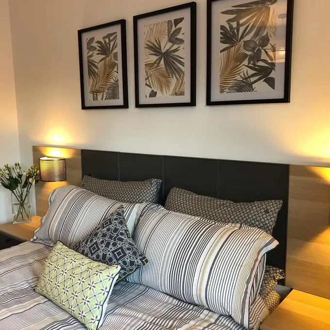 IKEA panelleri, entegre komodinler ve aydınlatma ile otel tarzı bir yatak başlığına dönüştürülmüş. Temiz hatlar, parçalar basit olsa da özel tasarım hissi veriyor.