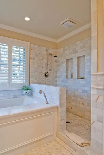 Mermer fayanslı şık banyo, duş alanında alçak duvar ve panel kaplı küvet.