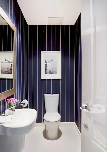 Lacivert ve beyaz ince çizgili duvar kağıdı, beyaz duvara monte lavabo ve sanat eseri bulunan küçük misafir tuvaleti.