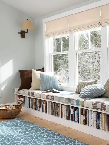 Açık depolama bankı, rahat bir daybed ve kitap rafları sağlayan tam bir okuma köşesi.