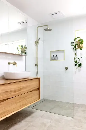 Beyaz ve gri karolarla modern küçük banyo, ahşap lavabo, ayna dolap ve pirinç detaylarla tamamlanmış.