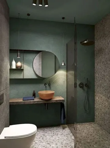 Yeşil duvar, terrazzo zemin ve duvar, ahşap asma lavabo ve mercan rengi kurna ile yaratıcı küçük banyo.