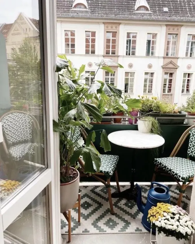 Balkon, hasır sandalyelerle oturma alanı, bolca çiçek ve bitki sunuyor.