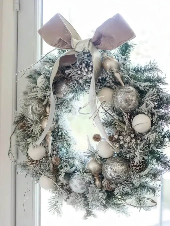 Kar kaplı kozalaklar ve üstte bir kurdele bulunan gümüş Noel çelengi, şık ve elegan bir yılbaşı dekor fikri.