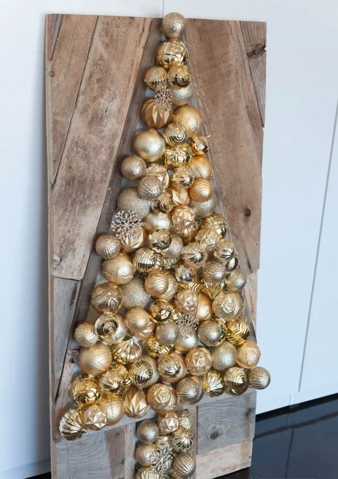 Bu palet ahşap tabela, mekâna şıklık ve gösteriş katan altın renkli süslerden oluşan bir Noel ağacı gösteriyor.