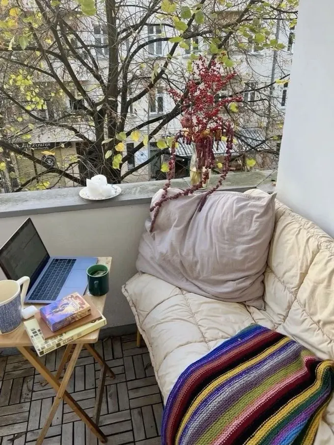 Balkon, küçük bir kanepe, masa olarak katlanabilir tabure, birkaç mum ve battaniyeyle çalışma alanına dönüştürülmüş.