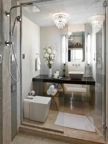 Küçük ve zarif banyo, taş karolar, kristal avize, duş alanı ve gömme koyu renkli lavabo ile tasarlanmış.