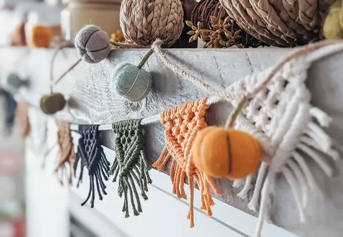 Bej, yeşil ve turuncu gibi toprak tonlarındaki makrome üçgenler ile pastel renklerde keçe top kabakların birleşimi, mükemmel bir bohem sonbahar garlandı sunuyor.