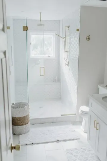 Büyük ve balık pulu desenli beyaz karoların kullanıldığı küçük beyaz banyo, duşta beyaz lavabo, sepet ve altın armatürler.